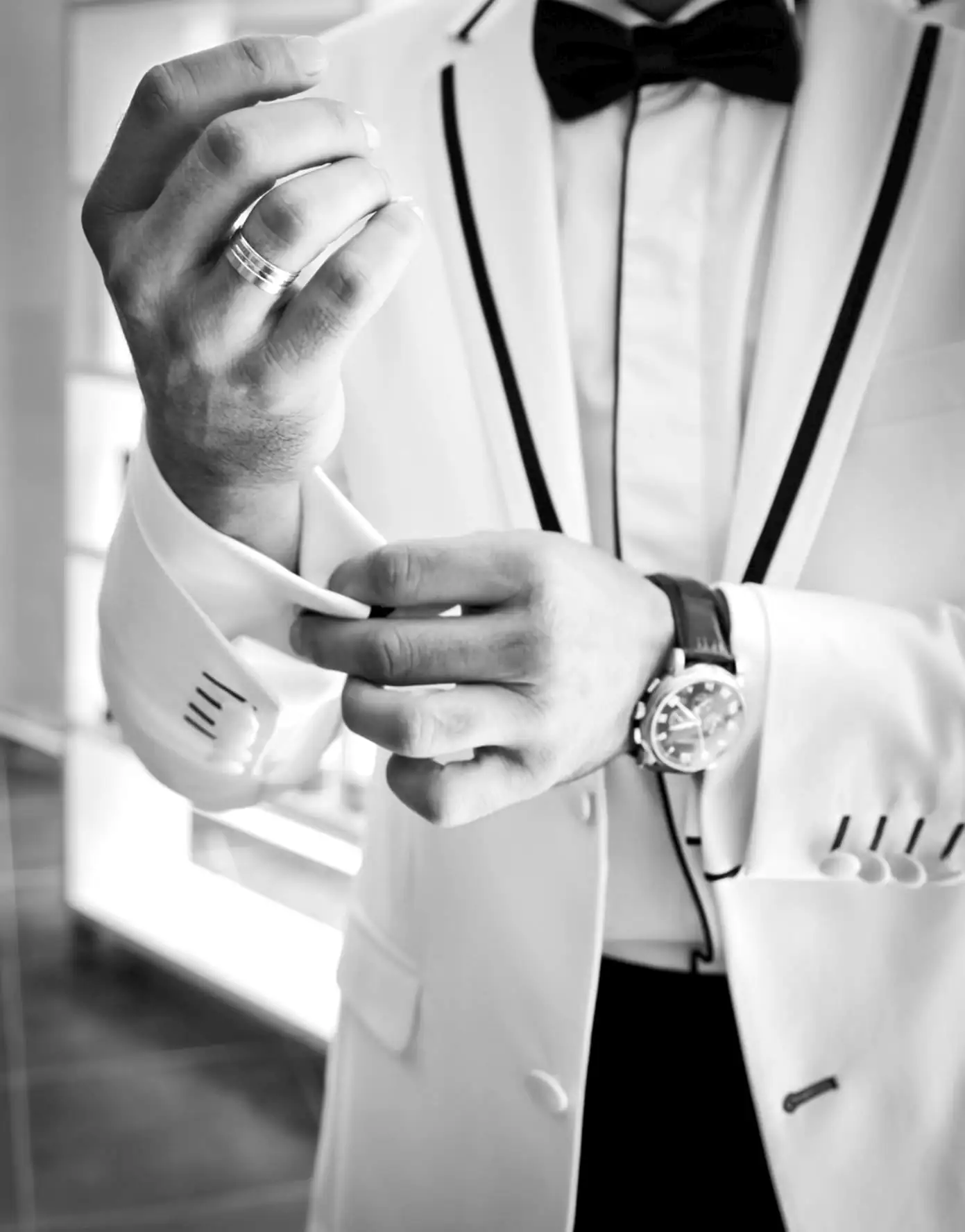 Black and white: a man in a white dinner jacket and black bow tie fastening his shirt cuff