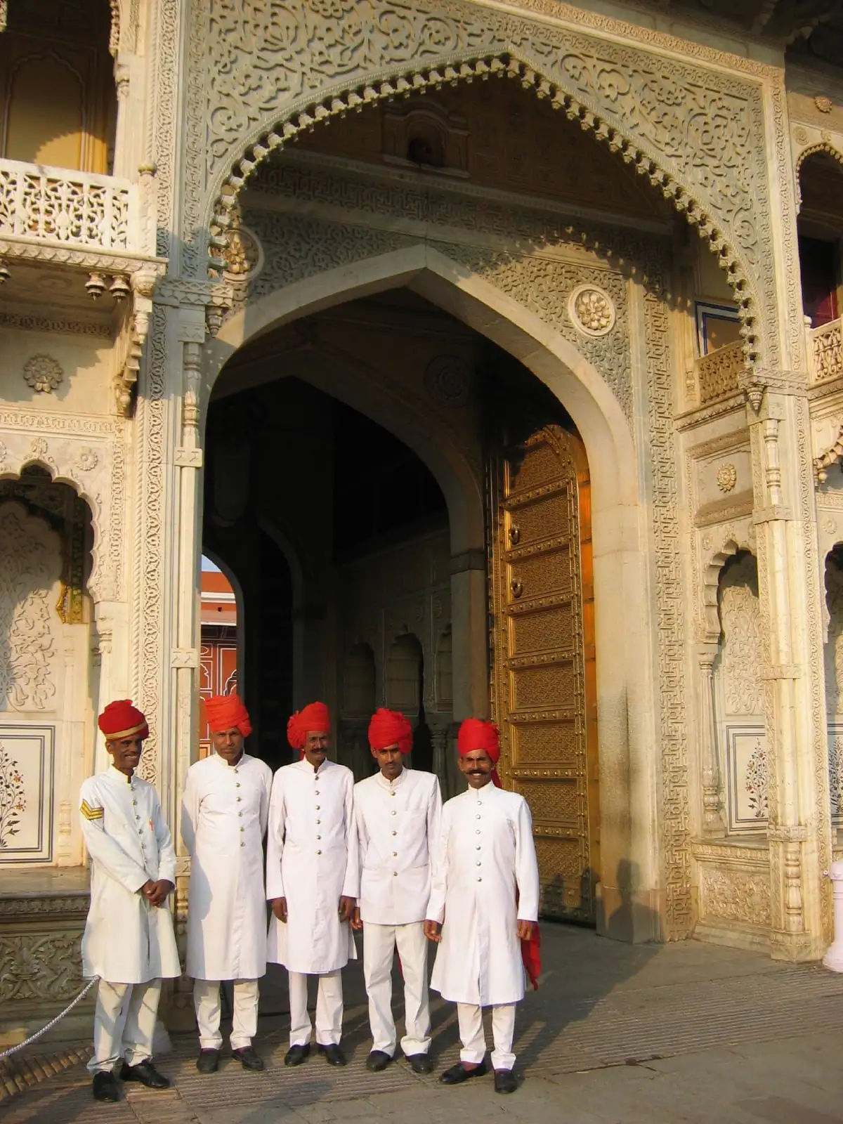 Palace attendants in red safas beneath a carved gateway